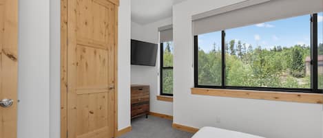 Une chambre avec une grande fenêtre, une armoire en bois, un téléviseur et un sol recouvert d’une moquette.