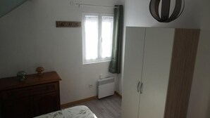 Makuuhuone, jossa on sänky, vaatekaappi, patteri, ikkuna, jossa on verhot, ja katosta roikkuva valaisin.