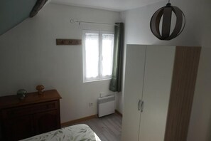 Een slaapkamer met een bed, een kledingkast, een radiator, een raam met gordijnen en een hanglamp.