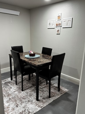 A dining area with a marble table, black chairs, a rug, and framed artwork on the wall.