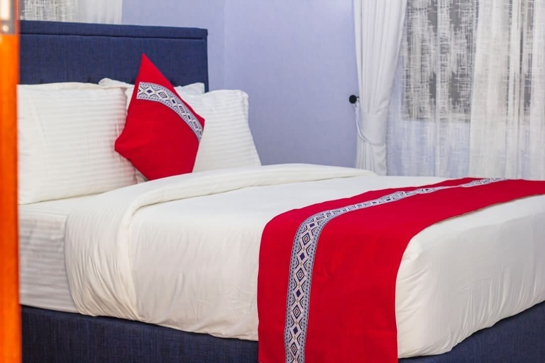 Una cama con ropa de cama blanca y una colcha roja, un cabecero azul y un almohadón rojo con un diseño blanco.