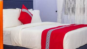 A bed with white bedding and a red blanket, a blue headboard, and a red pillow with a white pattern.