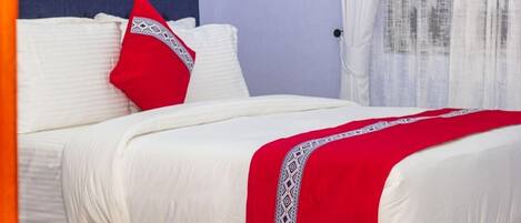 Una cama con ropa de cama blanca y una colcha roja, un cabecero azul y un almohadón rojo con un diseño blanco.