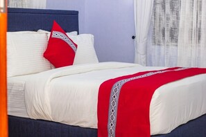 A bed with white bedding and a red blanket, a blue headboard, and a red pillow with a white pattern. - Moonlight Hotel (Dar es Salaam)