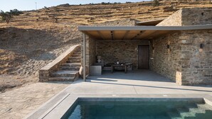 Un edificio de piedra con piscina, asientos al aire libre y una escalera que sube por una ladera.