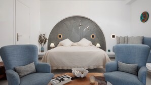 Un dormitorio moderno con una cama grande, dos sillones, una mesita de noche y un elemento decorativo en la pared.