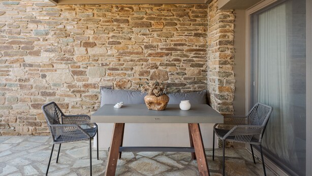 Un muro de piedra, una mesa con dos sillas y una ventana con cortinas.