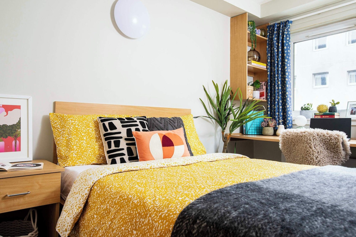 A neatly arranged bedroom with a bed, bedside table, and a desk with a chair.