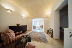 Un vaste espace de vie comprenant un canapé, une table en verre avec un verre à vin, un tapis à motifs et une vue sur une autre pièce où se trouvent un canapé et un fauteuil.
