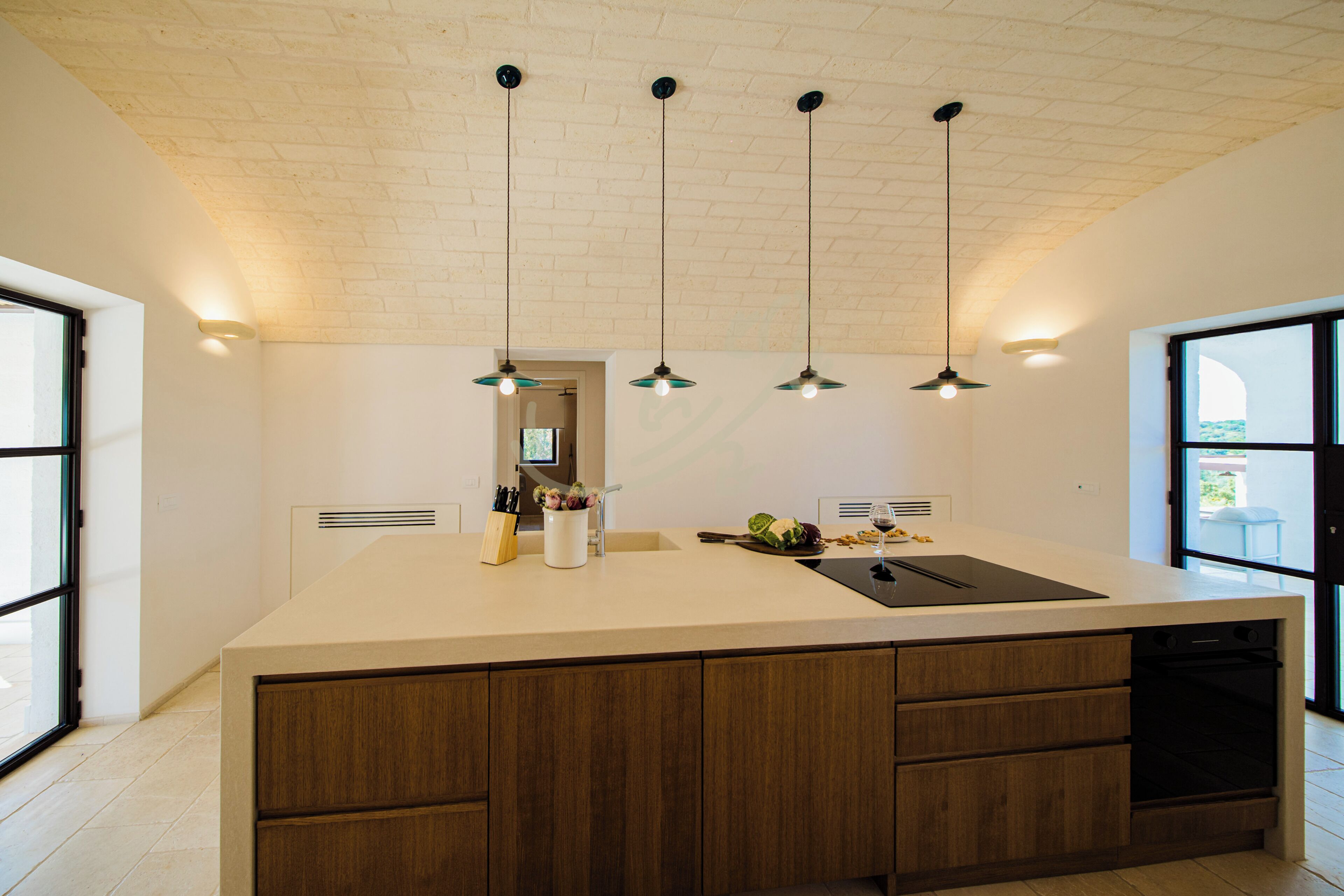 Una cocina moderna con una isla grande, iluminación colgante y vistas al exterior.
