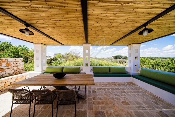Une terrasse extérieure avec une table en bois, des chaises en osier et des sièges rembourrés de couleur verte.