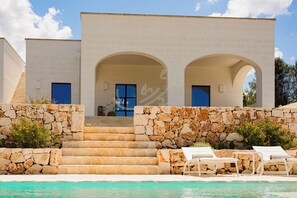 Un bâtiment moderne doté d’une piscine, d’un escalier en pierre et de deux portes cintrées.