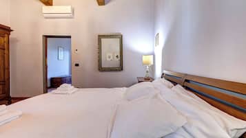 A hotel room with a bed, a nightstand, a lamp, a mirror, and a door leading to another room.