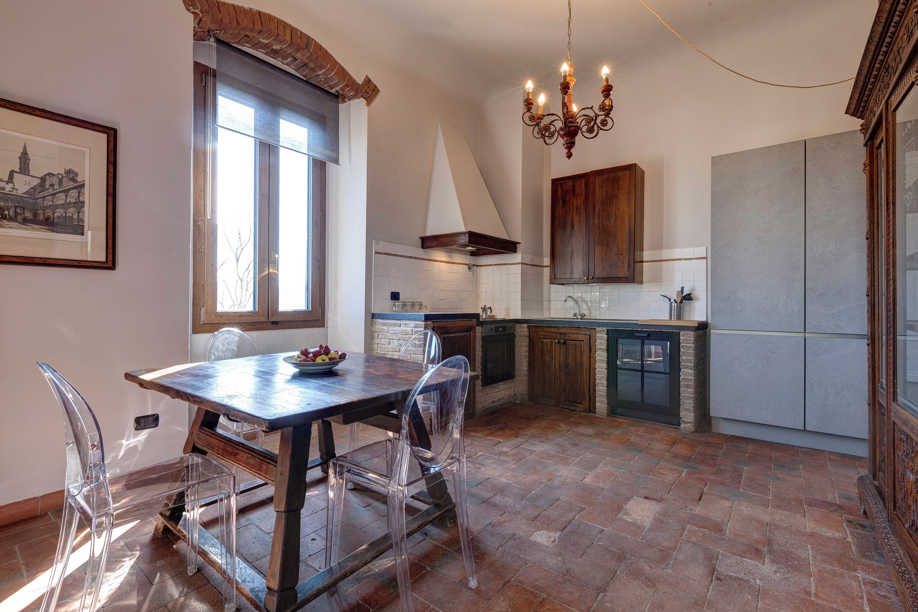 A kitchen with a dining table, chairs, a chandelier, and a large window.