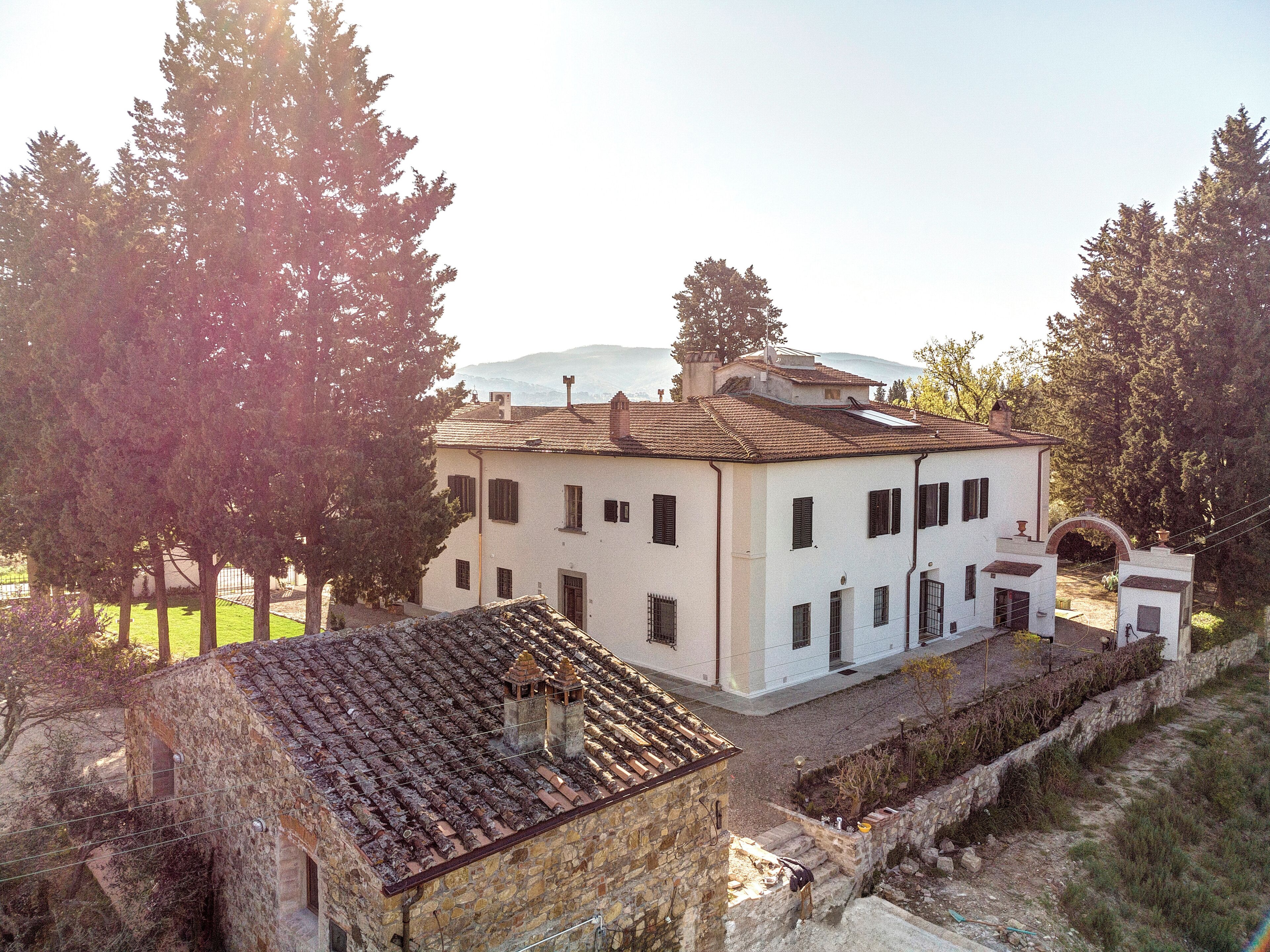 A two-story building with a tiled roof, a stone wall, and a small garden area.