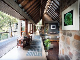 A spacious interior with a high ceiling, a wooden staircase, and a balcony overlooking greenery.