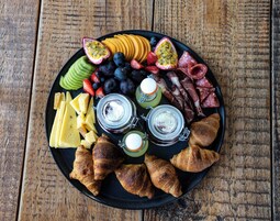 Una tabla de quesos y embutidos con varias opciones de quesos, frutas y carnes sobre una mesa de madera.