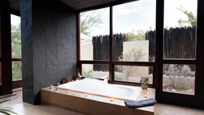 Un cuarto de spa con una bañera grande, una ventana con vistas a árboles y una pared de piedra.