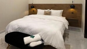 A modern hotel room with a large bed, a ceiling fan, an air conditioning unit, and a bench with a towel. - Address 12 Apartments Model Town Lahore (Lahore)