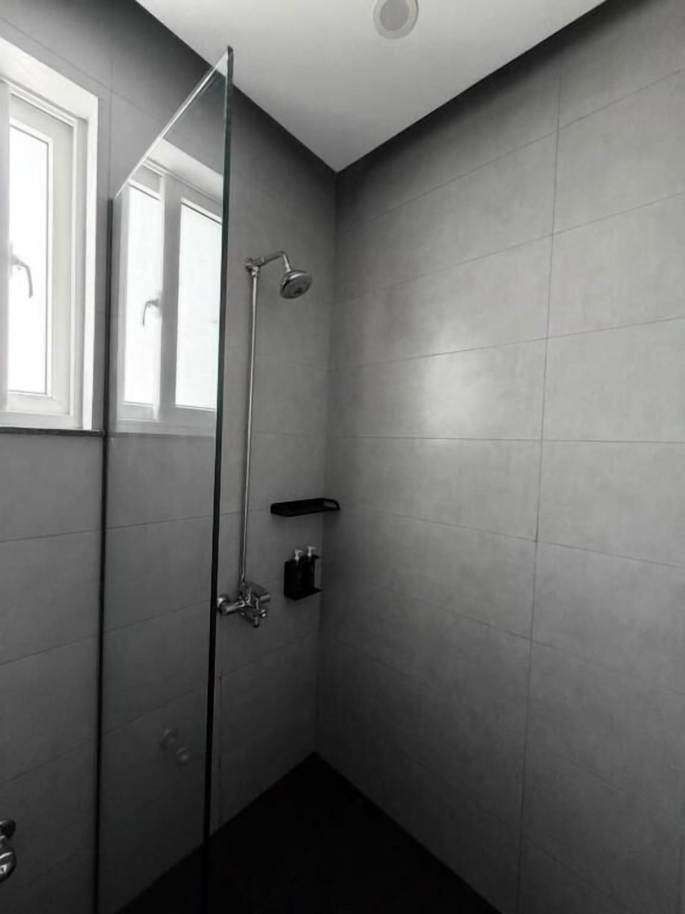 Una ducha moderna con puerta de vidrio, ventana y un pequeño estante con artículos de aseo.