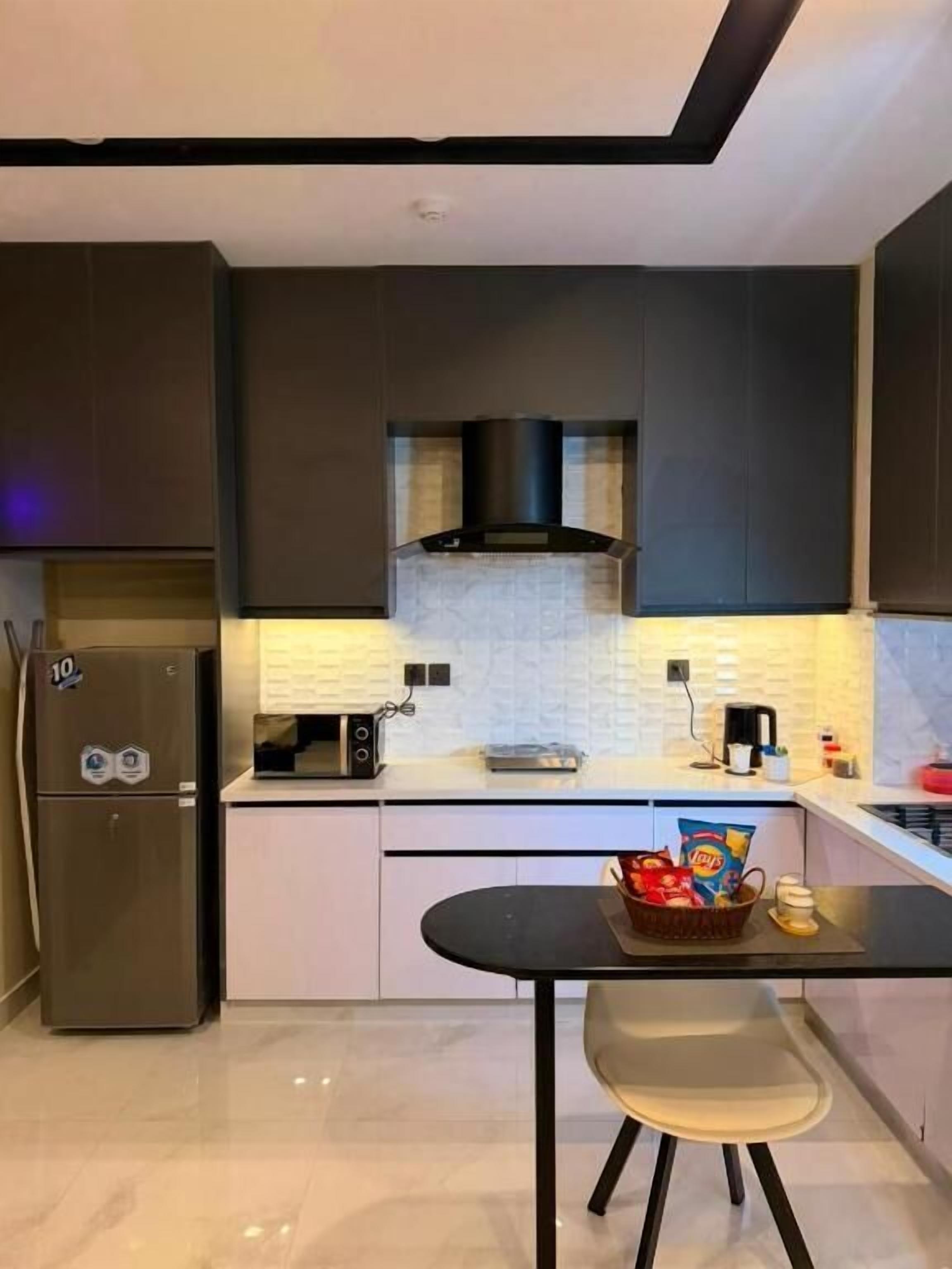 A modern kitchen with dark cabinetry, a microwave, a toaster, and a small dining table with a basket of snacks.