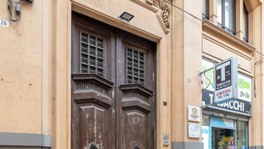 En bygnings facade med en stor trædør, et lille vindue med dekorativt jern og en butiksfacade med et skilt, der reklamerer for lotto.