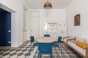 Ein modernes Wohnzimmer mit einem runden Tisch, blauen Stühlen, einer Couch und einer Küchenzeile mit Schränken.