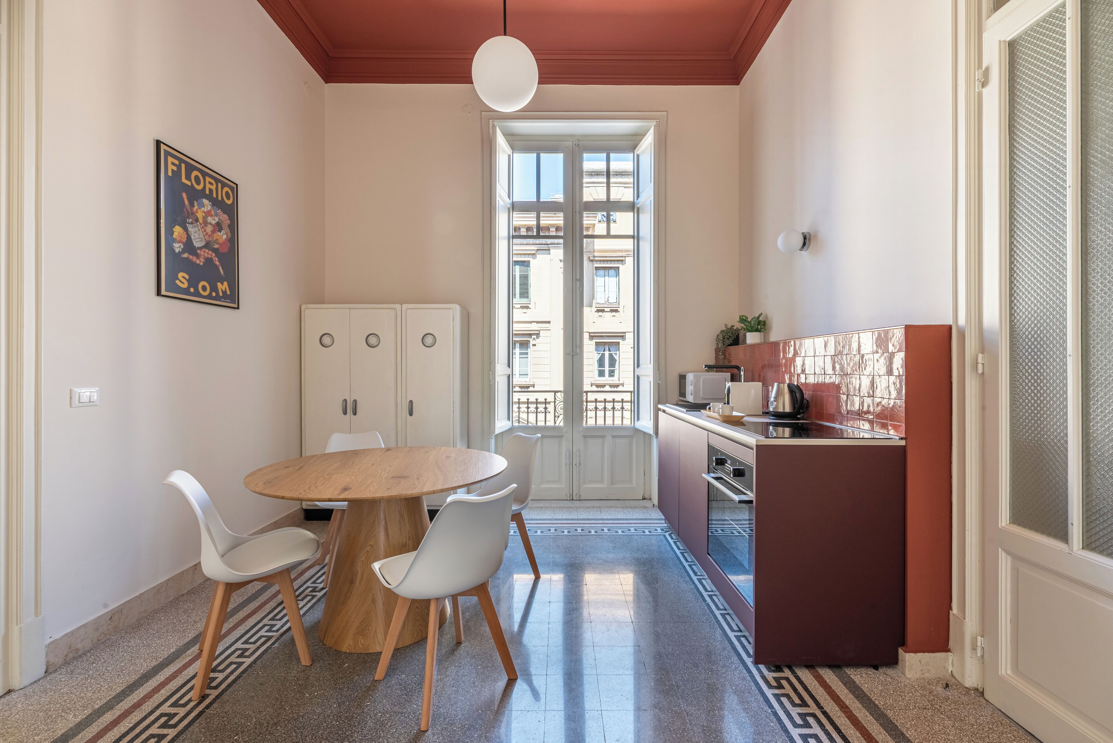 A compact kitchen with a dining area, featuring a round wooden table, white chairs, and a small refrigerator.