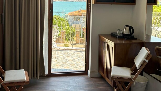 Een hotelkamer met een bed, twee stoelen, een bureau met waterkoker, een televisie en uitzicht op zee.