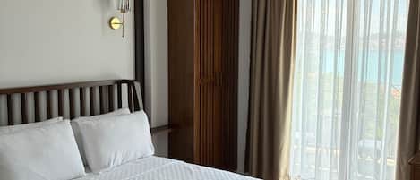 A hotel room with a large bed, a wardrobe, a chandelier, and a view of the outdoors.