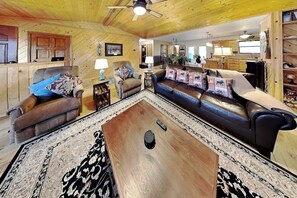 A cozy living room with a wooden ceiling, a brown leather sofa, a matching armchair, and a coffee table. - Casa Aurora | Serene Sanctuary + Large Deck (Ruidoso)
