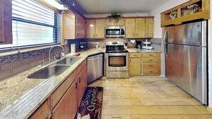 Een keuken met houten kastjes, roestvrijstalen apparatuur, een granieten aanrechtblad en een raam met blinds.