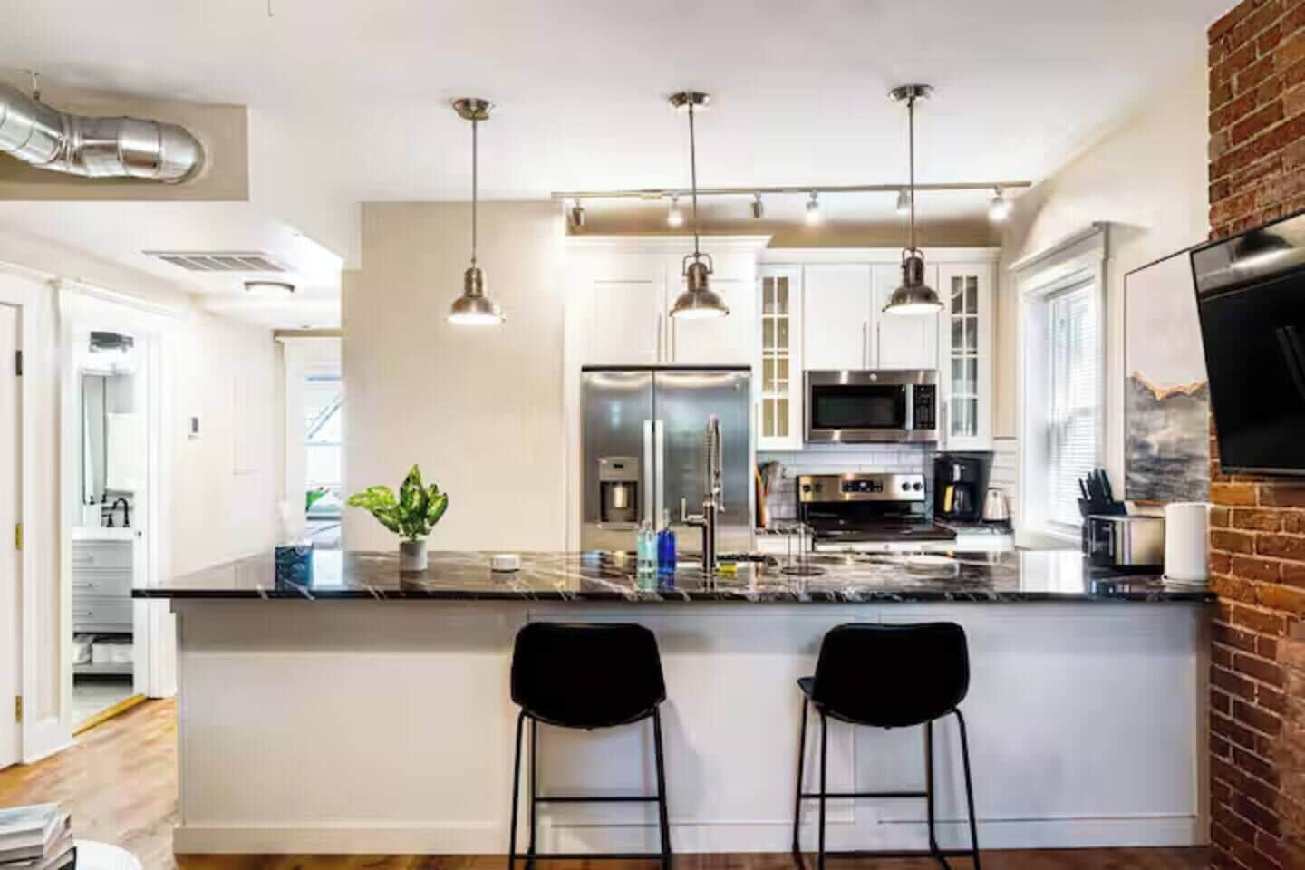 A modern kitchen with a central island, pendant lighting, stainless steel appliances, and a brick accent wall.