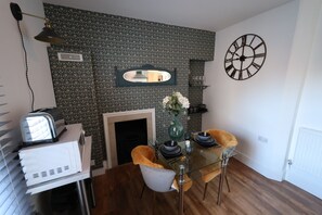 A dining area with a glass table, two chairs, a vase with flowers, a clock, and a fireplace. - Stylish apartment with en-suite and kitchen/ dining room. (Whitby)