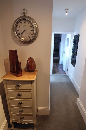 A hallway with a wall-mounted clock, a wooden dresser with drawers, and a vase. - Stylish apartment with en-suite and kitchen/ dining room. (Whitby)