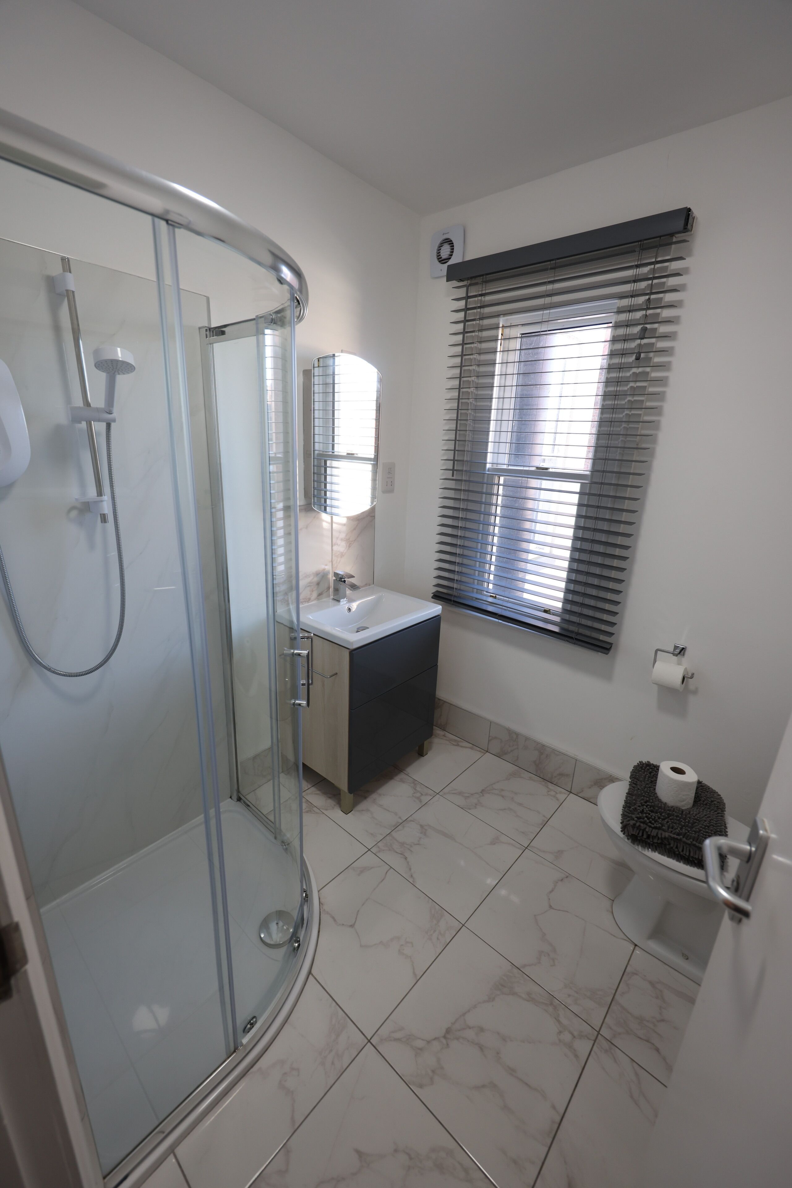 A modern bathroom with a glass-enclosed shower, a sink with a mirror, and a toilet with a paper holder.
