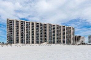 Ein Hochhaus-Hotel mit mehreren Etagen und Balkonen, gelegen an einem Sandstrand unter blauem Himmel.