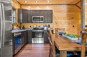 A compact kitchen with dark cabinets, stainless steel appliances, and a wooden dining table with chairs. - Smoky Ridge Retreat 4 Bedroom Cabin (Sevierville)
