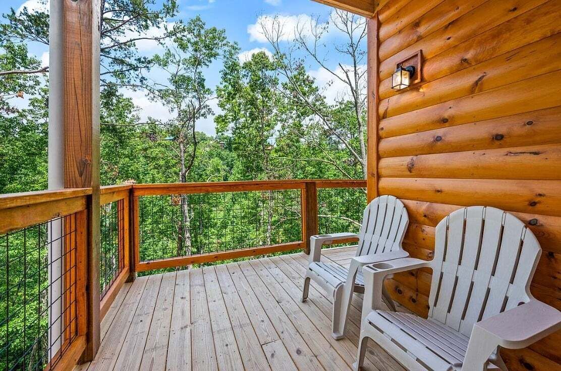 Una terraza de madera con dos sillas Adirondack blancas y vista a un bosque.
