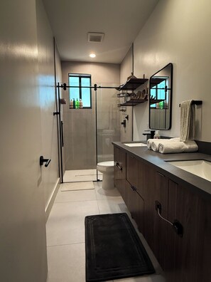 Ein modernes Badezimmer mit Duschkabine aus Glas, Toilette, Waschtisch mit Spiegel und einem Fenster für natürliches Licht.