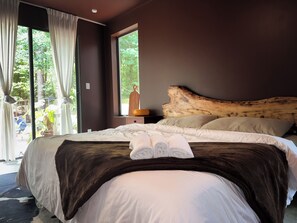 Ein Schlafzimmer mit einem großen Bett, einem Holzkopfende und Blick auf Grün.