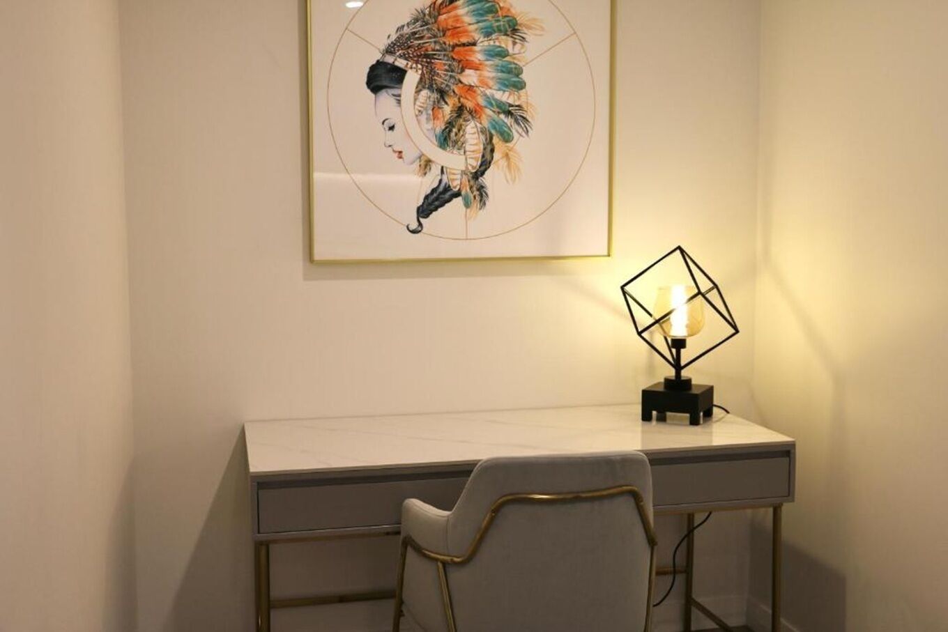 Een bureau met een stoel, een wandlamp en een lijst met een kunstwerk.