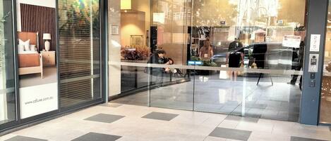 Entrada de um hotel com porta de vidro, uma placa da Cdluxe Interior Australia e piso ladrilhado.