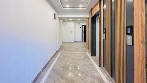 Un pasillo con suelo de mármol, paneles de madera en las paredes y un ascensor con pantalla digital.