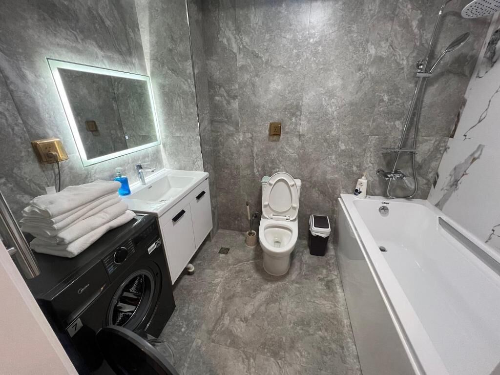 A bathroom with a washing machine, toilet, and bathtub.