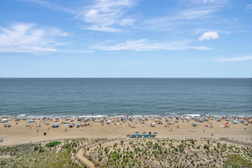 A beach with a fence, beach umbrellas, and a clear sky.