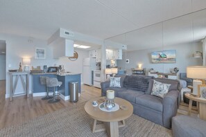 A modern living room with a grey sofa, a coffee table, and a kitchen area with a bar.