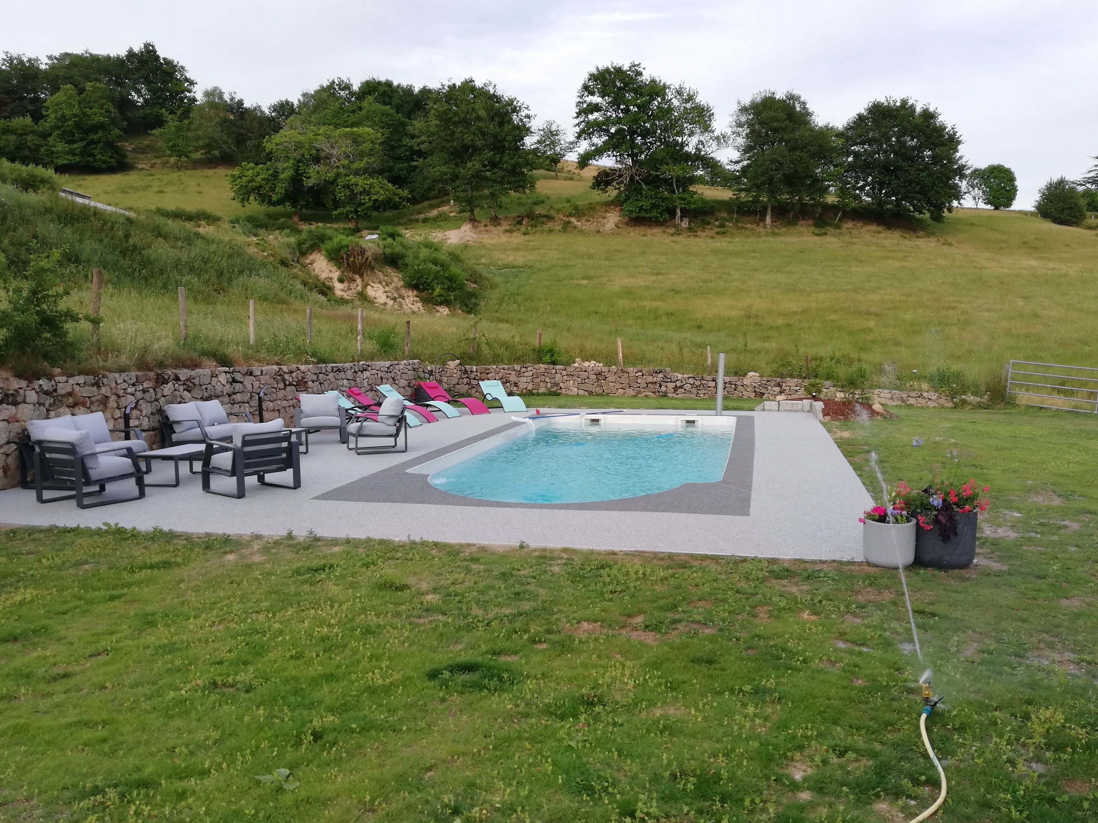 A backyard with a swimming pool, lounge chairs, and a stone wall.