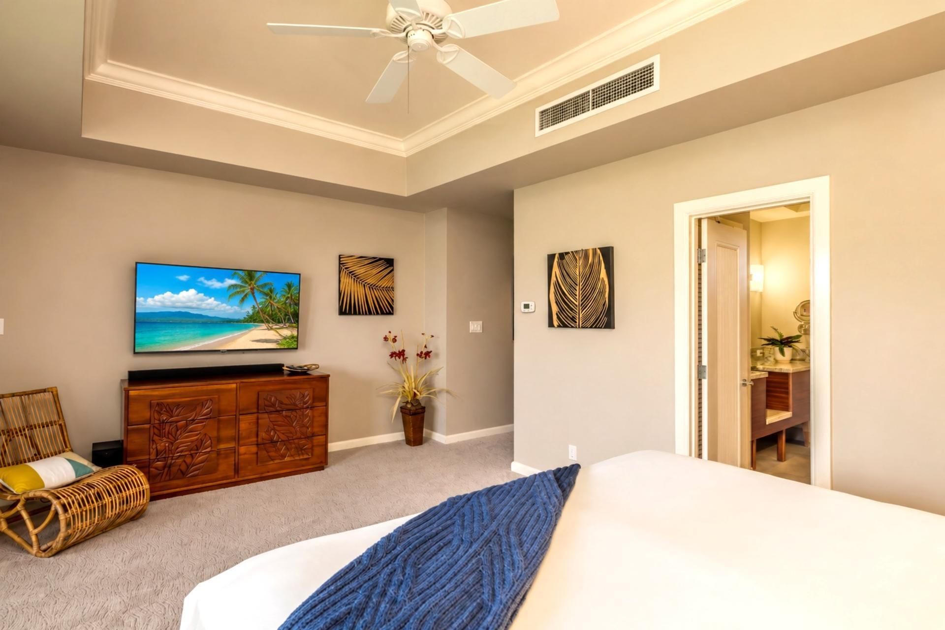 A bedroom with a bed, a television, a ceiling fan, and artwork on the walls.