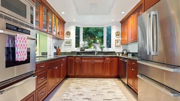 Een moderne keuken met houten kastjes, roestvrijstalen apparatuur en uitzicht op groen.